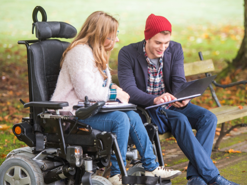 woman in motorized wheelchair speaking with young man with red toque outside